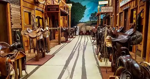 Main Street with saddles on hitching rails in front of old west buildings.