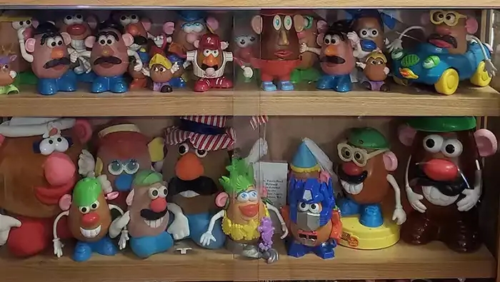 Two shelves displaying dozens of different sized potato head dolls. 