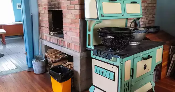 Old turquoise and white wood-burning stove in front of a huge chimney with an open oven. 