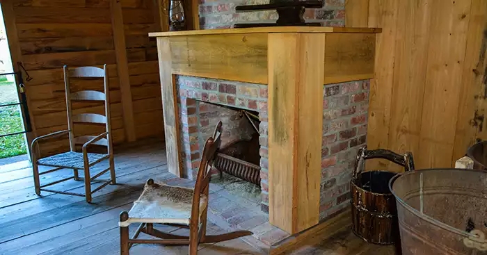 Old brick fireplace, washtub, pail, chairs and lantern in a worker cabin. 