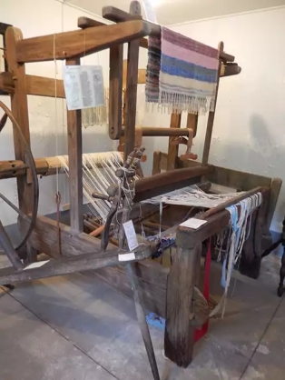 Rocker beater loom with rug made on it on display, as well as threads. 