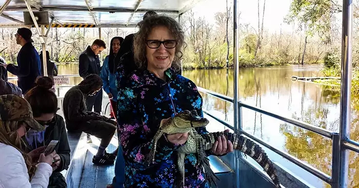 Linda Aksomitis holding a small alligator on a swamp boat in the Bayou. 