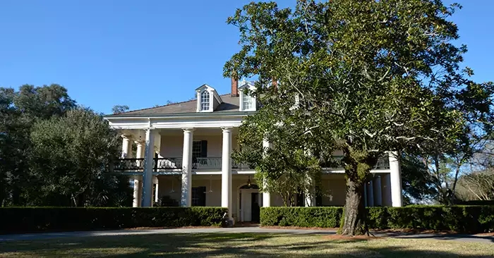Large white plantation house with a large tree in front