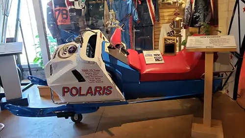 1970 Polaris with white hood, red seat, and blue sides, along with gear worn by the thrill team. 