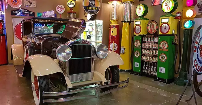 A cream colored vintage car is the focal point with lots of service station elements around it. 