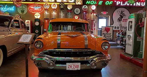 Orange vintage car is the focal point, with things like old gas pumps and petroleum collectibles. 