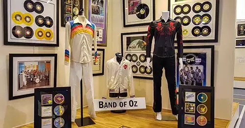 A man's white costume and black costume, along with a jacket. Walls are covered with old '45 albums and photos. 
