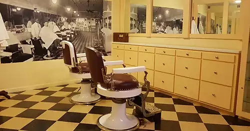 Focal point is two barber chairs with historic photo on wall and row of cupboard drawers. 