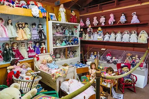 Shelves of dolls propped up as well as various dolls in cradles, baskets, and children's chairs. 