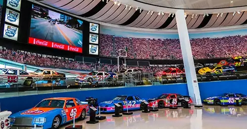 Built to replicate an oval race track, the entrance has two rows of race cars, one above the other, with a full size graphic of fans behind on the wall. 