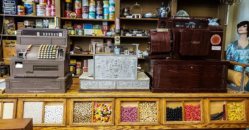 Three cash registers from various eras with bins of different types of candy. 