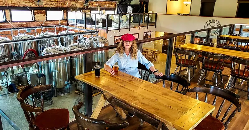 Linda Aksomitis in the tasting room with the beer vats on a lower level